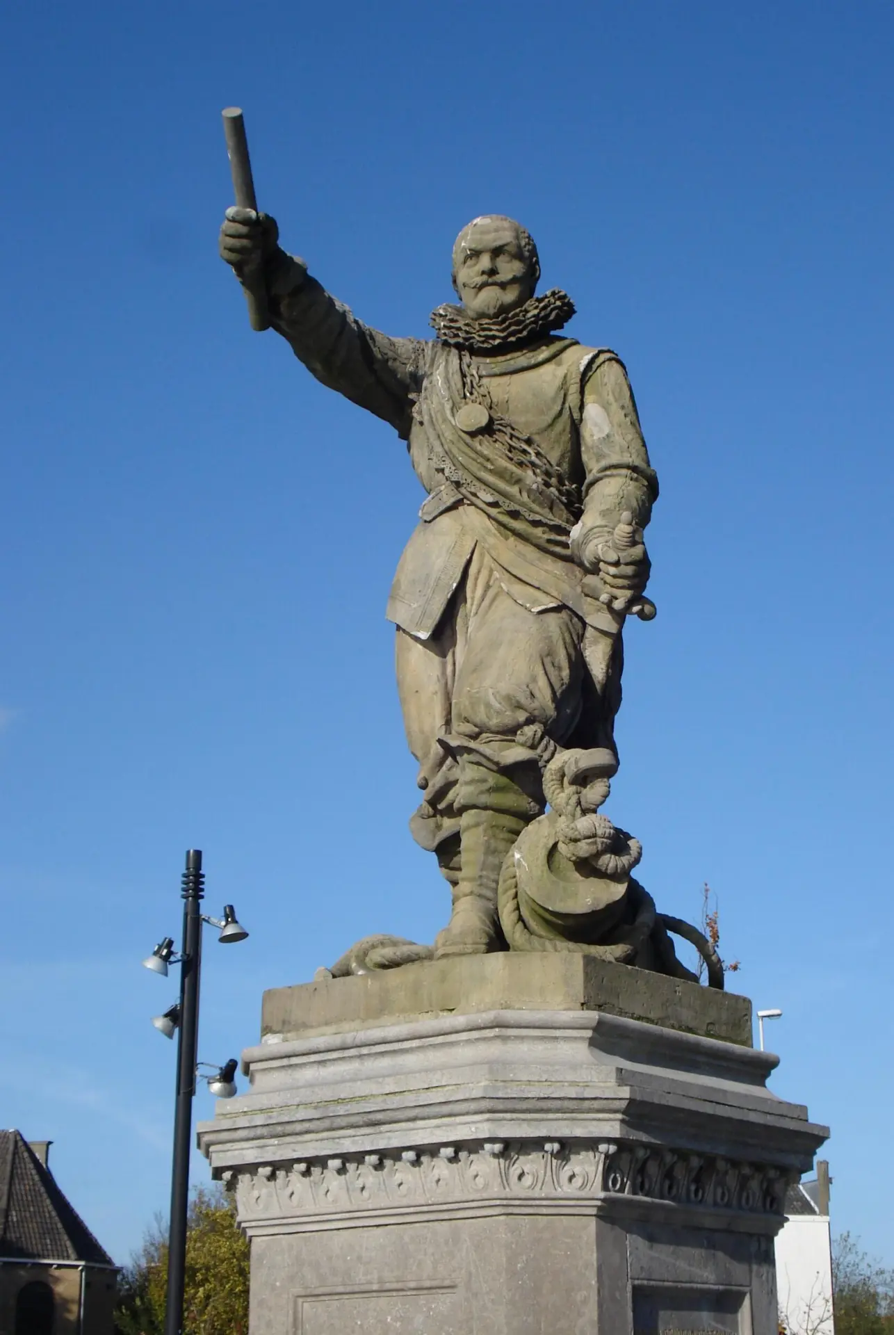 Stone statue of Piet Heyn on a plinth, baton raised, against a blue sky